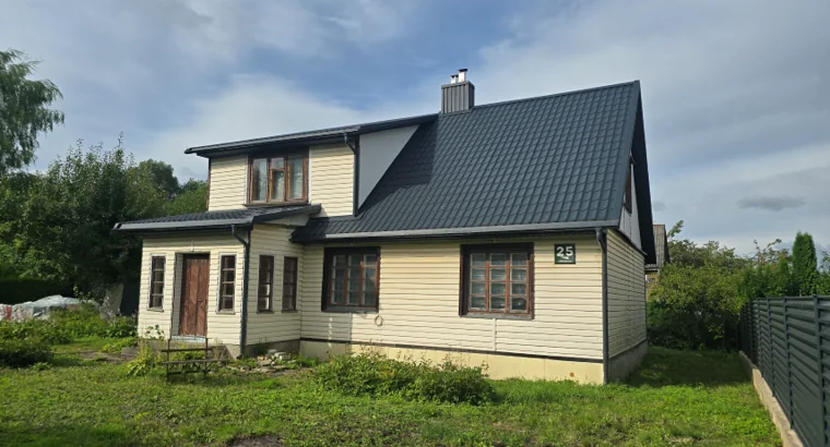 A pale wooden house with a dark roof and the number 25 beside its front windows.