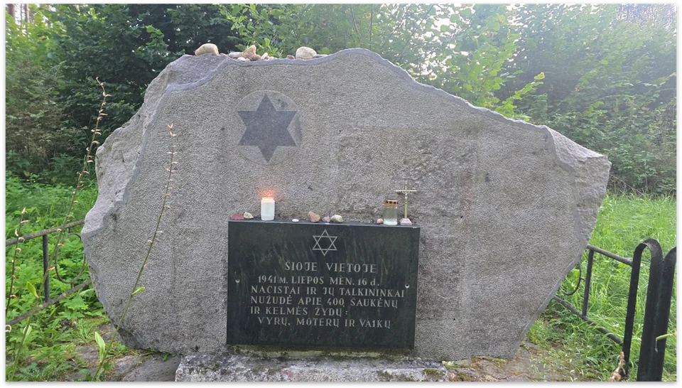 Memorial stone bearing a Star of David and an inscribed plaque, with small stones and a lit candle.